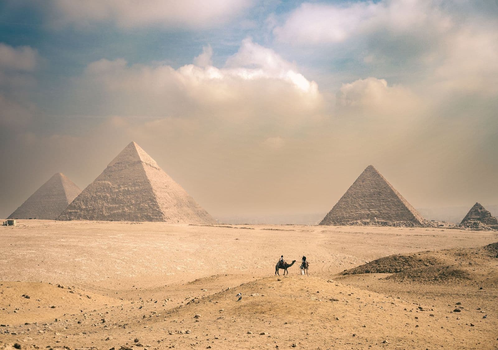 Camel riders crossing the desert before the pyramids of Giza