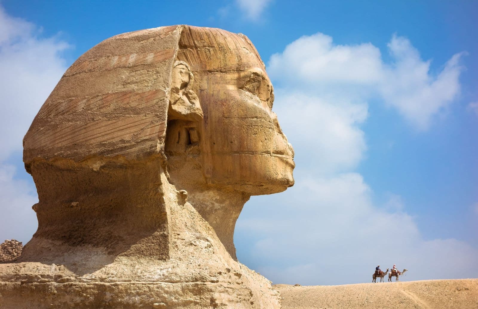 Side view of the Great Sphinx's head against a blue sky with white clouds