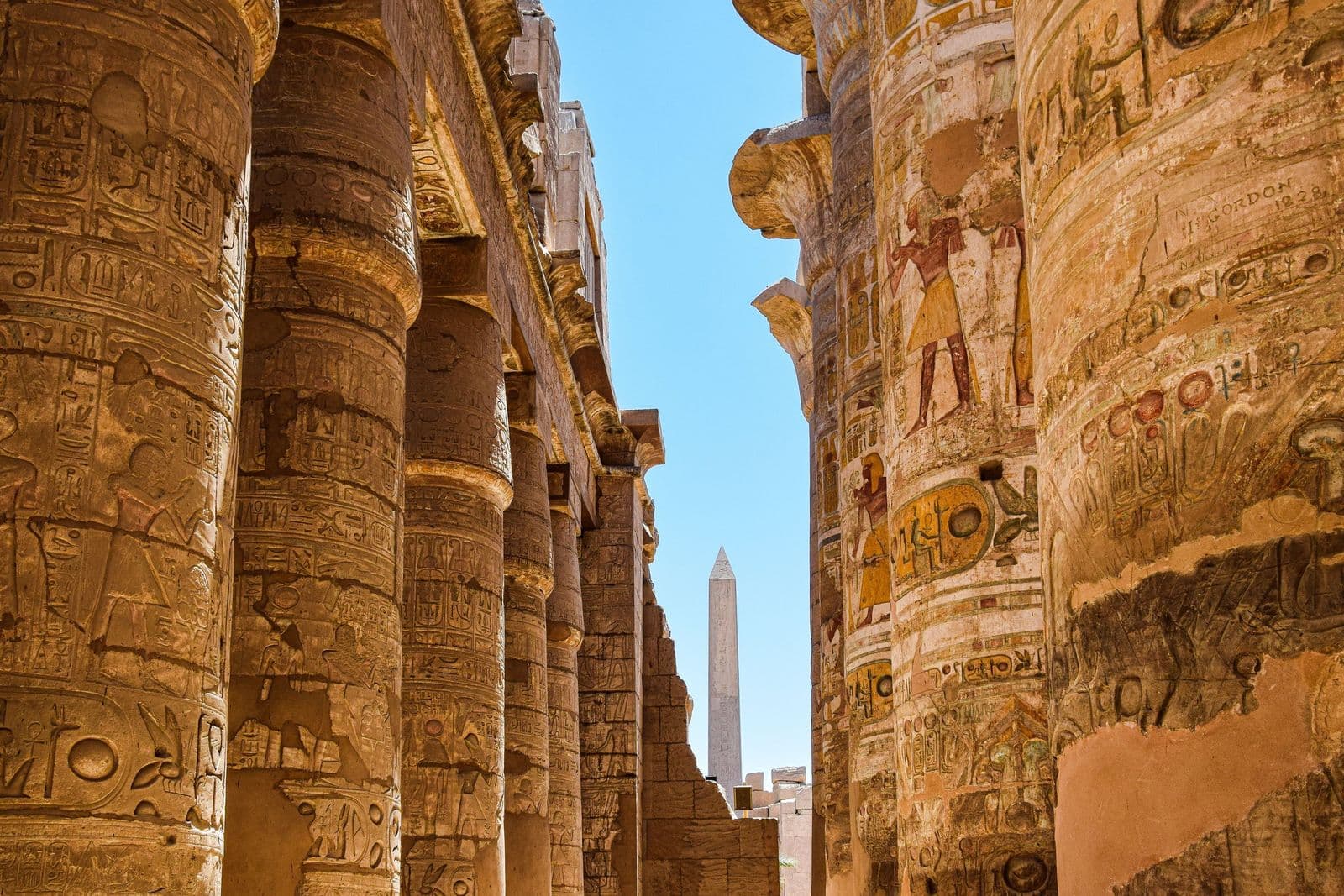 Painted columns of Karnak Hypostyle Hall with an obelisk in the distance