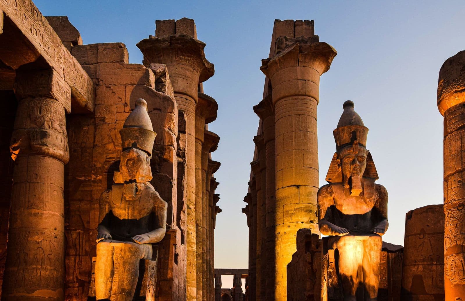 Seated statues of Ramesses II glowing at dusk inside Luxor Temple