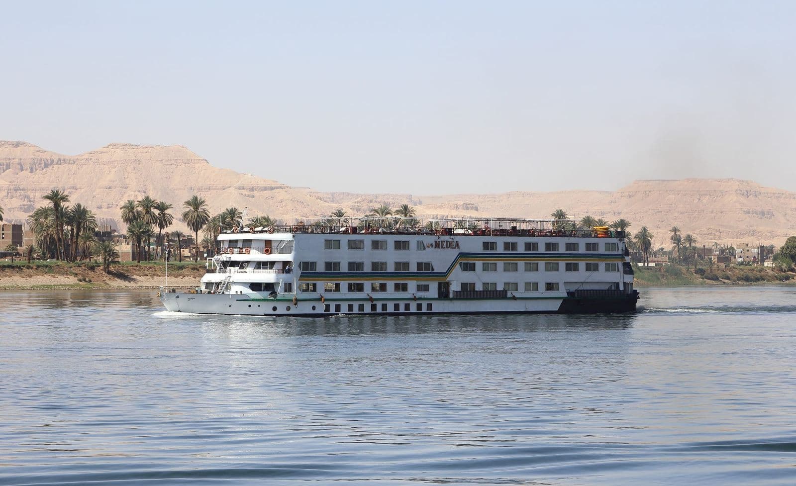 A Nile cruise ship sailing past palm trees and the Theban hills near Luxor