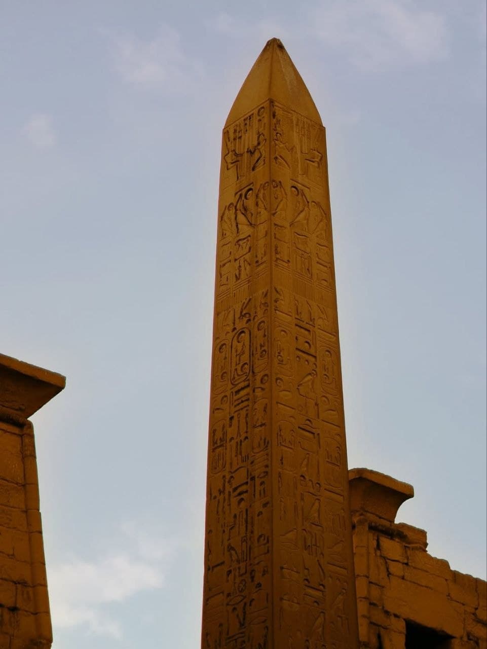 A granite obelisk covered in hieroglyphs beside a temple gateway in Luxor