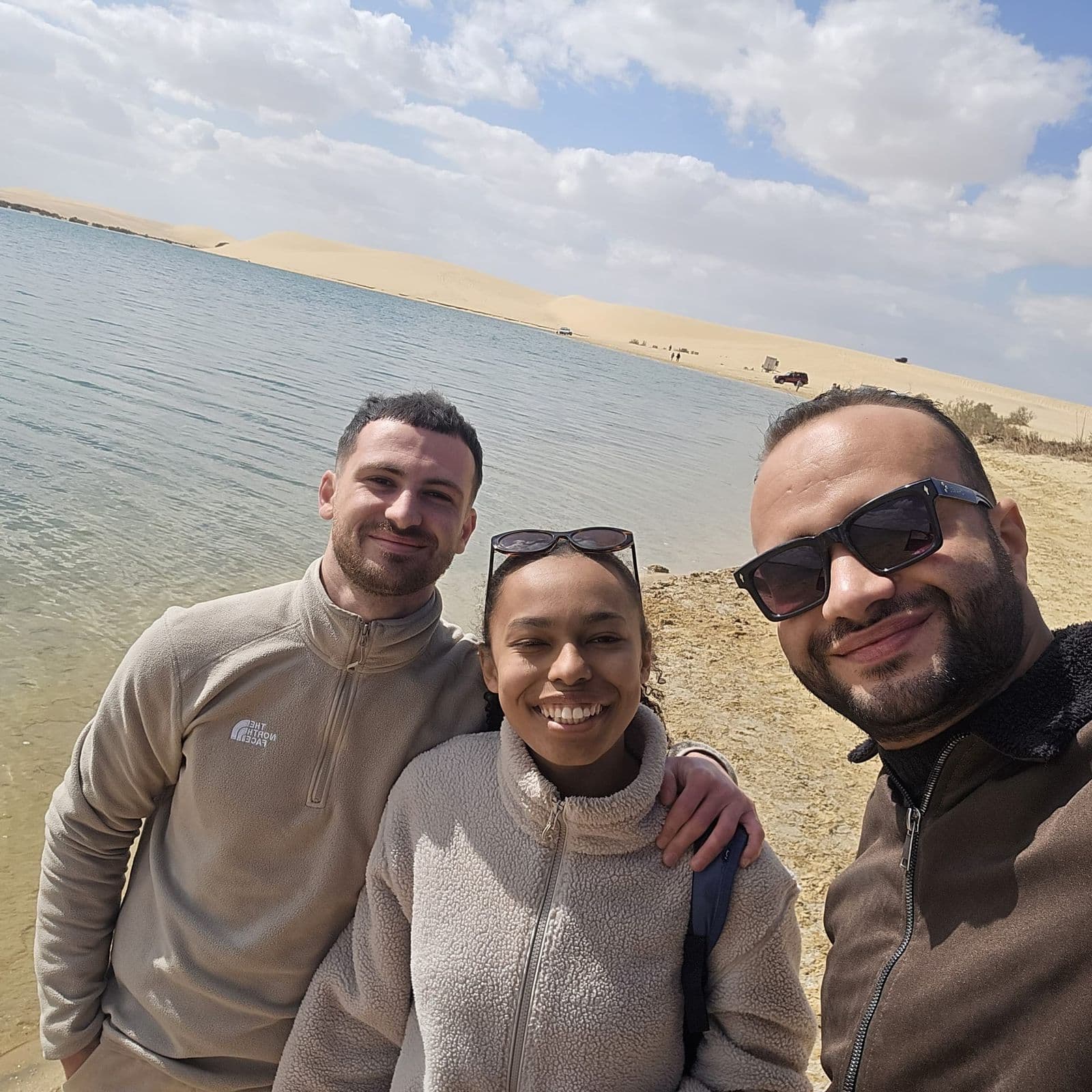 Tarek with two travelers on the shore of Magic Lake, Fayoum, with dunes behind