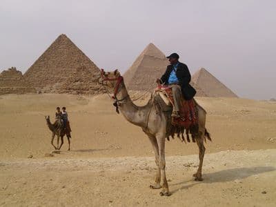 A camel rider on the sand with the three Pyramids of Giza behind