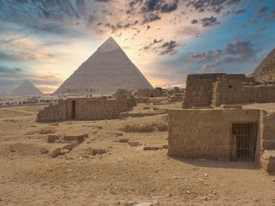 Pyramids of Giza and ancient stone tombs beneath a colourful sunset sky