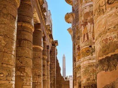 Painted columns of Karnak Hypostyle Hall with an obelisk in the distance