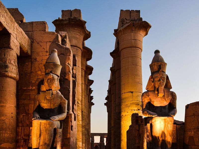 Seated statues of Ramesses II glowing at dusk inside Luxor Temple